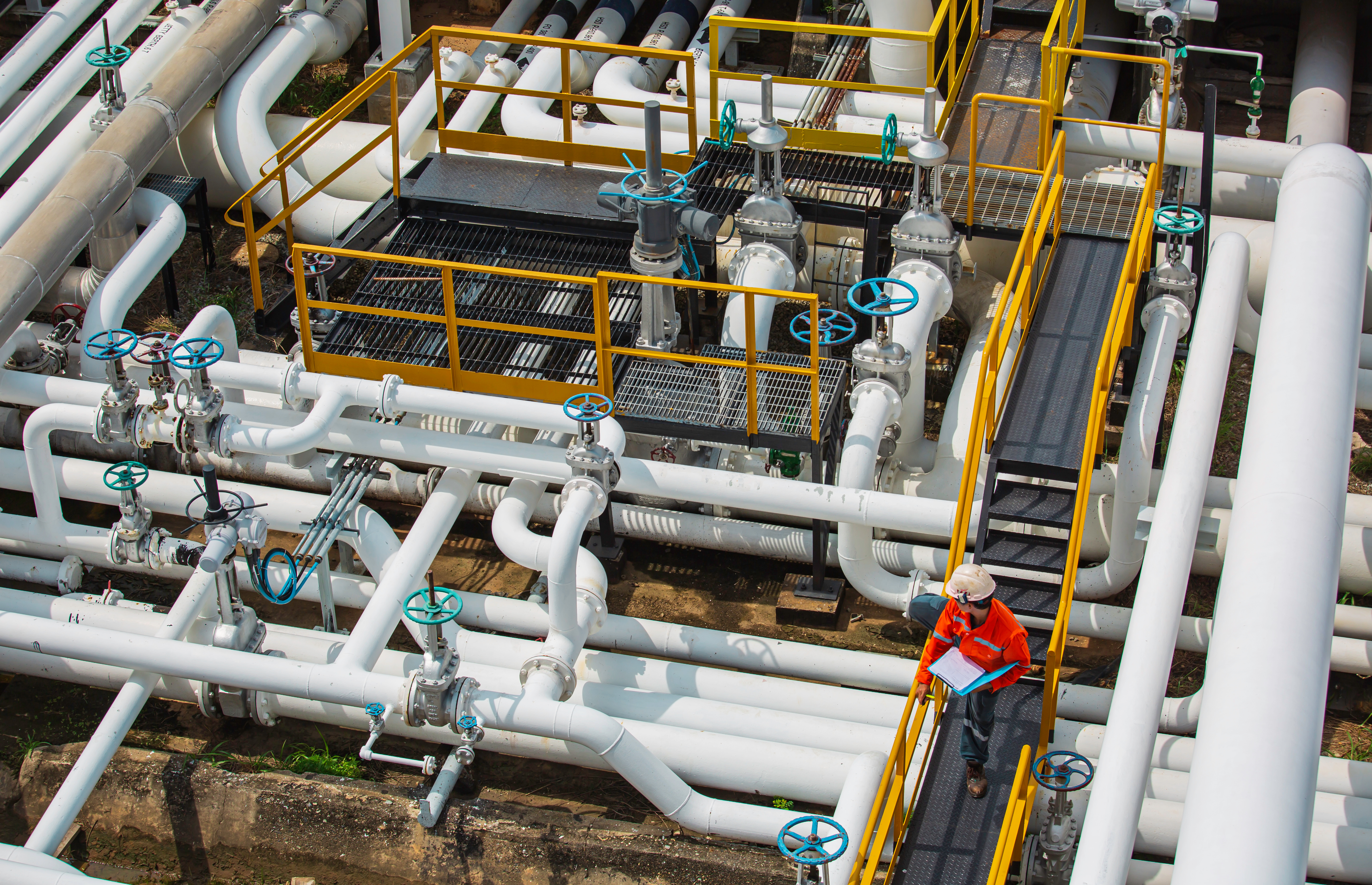 Engineer inspecting an industrial processing facility with complex piping systems, representing regulatory compliance and operational oversight.